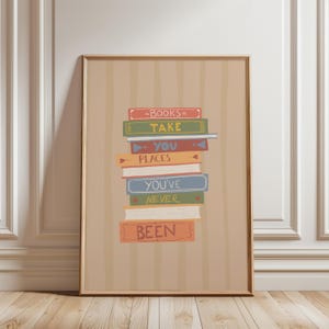 May include: A framed print showing a stack of books in various colours. Each book has text that reads "BOOKS TAKE YOU PLACES YOU'VE NEVER BEEN". The background is light brown with vertical stripes, and the frame is brown.