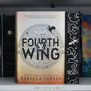 Puede incluir: Un libro titulado "Fourth Wing" de Rebecca Yarros. La portada presenta una ilustración en blanco y negro de un dragón volando a través de nubes con un diseño circular a su alrededor. El libro está en un estante con otros libros.