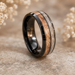 May include: A black metal ring featuring a central inlay composed of two distinct sections of textured, fibrous material in shades of light tan and off-white, set within a polished, dark, reflective band with beveled edges.