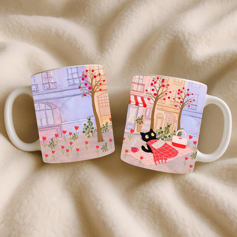 May include: Two white ceramic mugs with a whimsical illustration. The design features a black cat enjoying a picnic in a city park setting. The scene includes trees with red berries, buildings, and a red and white blanket.