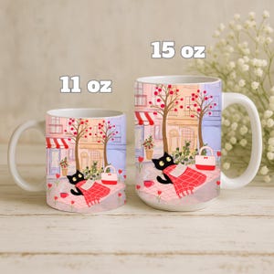 May include: White ceramic mugs with a whimsical illustration of a black cat relaxing on a blanket in a park setting. The mugs are available in 11 oz and 15 oz sizes, featuring a charming scene with trees, buildings, and a red and white picnic blanket.
