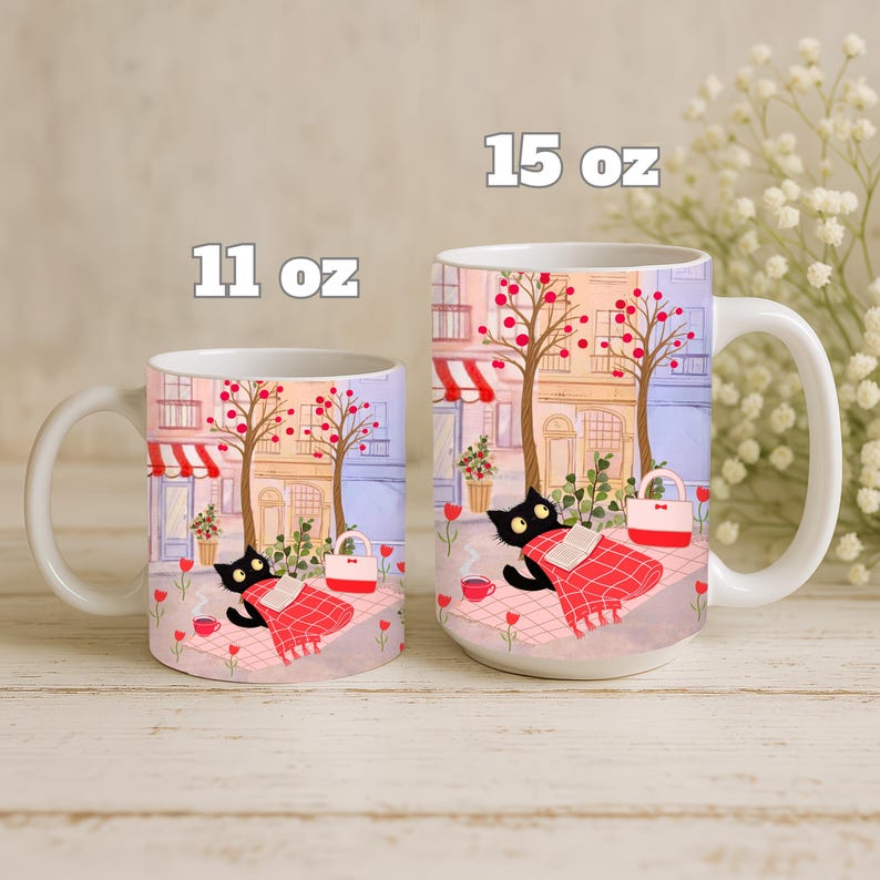 May include: White ceramic mugs with a whimsical illustration of a black cat relaxing on a blanket in a park setting. The mugs are available in 11 oz and 15 oz sizes, featuring a charming scene with trees, buildings, and a red and white picnic blanket.