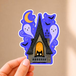 May include: A die-cut sticker featuring a black cat peering from a balcony of a tall, pointed-roof house. The scene includes a yellow crescent moon, two pale ghosts, and several black bats against a dark blue sky filled with small yellow stars.