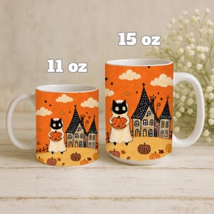 Puede incluir: Dos tazas de cer&aacute;mica blanca con una ilustraci&oacute;n naranja de Halloween de un gato disfrazado de fantasma sosteniendo una calabaza, junto a una casa encantada. La taza m&aacute;s peque&ntilde;a indica 11 oz y la m&aacute;s grande indica 15 oz.
