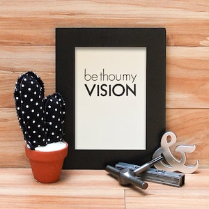 K&ouml;nnte beinhalten: Ein schwarzer gerahmter Druck mit den Worten "be thou my VISION" auf wei&szlig;em Hintergrund. Ein schwarz-wei&szlig; gepunkteter Kaktus in einem Terrakottatopf befindet sich links. Ein silbernes Et-Zeichen und ein Metallwerkzeug befinden sich rechts.