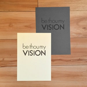 K&ouml;nnte beinhalten: Zwei rechteckige Karten mit dem Text "be thou my VISION" in fetter, schwarzer Schrift. Eine Karte ist cremefarben, die andere ist dunkelgrau. Die Karten liegen auf einer hellbraunen Holzoberfl&auml;che.