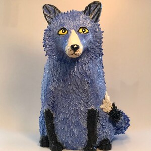 May include: A blue ceramic fox sculpture with black legs and a white patch on its side. The fox has yellow eyes and a white nose.