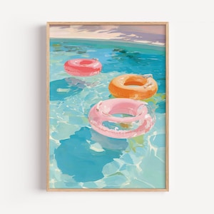 Op de afbeelding: Een ingelijste print met drie opblaasbare zwembanden in een zwembad. De banden zijn roze, oranje en rood en drijven in turquoise water. Het kunstwerk heeft een zomers vakantiethema.