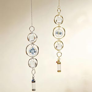 May include: Two hanging crystal suncatchers. One has silver-colored metal rings and chain, the other has gold-colored metal rings and chain. Both have clear crystal orbs and a small glass vial at the bottom. One has blue flowers inside a ring.