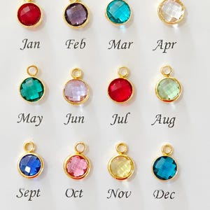 May include: Twelve gold-colored pendants with colorful, faceted gemstones, each representing a month of the year. The months are labeled Jan, Feb, Mar, Apr, May, Jun, Jul, Aug, Sept, Oct, Nov, and Dec.