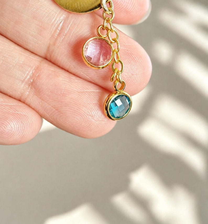 Puede incluir: Un componente de pulsera o collar de eslabones de metal dorado con dos piedras redondas facetadas en engaste de bisel. Una piedra es de color rosa transl&uacute;cido p&aacute;lido y la otra es de un azul transl&uacute;cido vibrante, suspendidas de una cadena dorada.