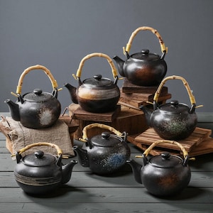 May include: A collection of black ceramic teapots with bamboo handles. Each teapot has a unique speckled or striped design in shades of brown, white, and blue. The teapots are displayed on small wooden platforms.
