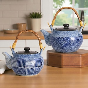 May include: Two blue and white ceramic teapots with bamboo handles. The teapots have black lids and are decorated with wave and geometric patterns. One teapot is on a wooden stand.
