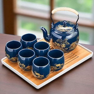 以下が含まれることがあります： 紺色の陶器製ティーセット。 ティーポットと、金色の風景模様で装飾された6つのカップが含まれています。 ティーポットには編み込みの取っ手があり、白い縁の竹製トレイの上に置かれています。 木製のテーブルに置かれています。