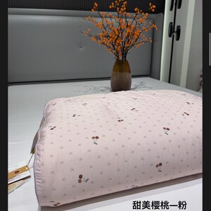 May include: A light pink pillow with a cherry pattern. The pillow is on a bed with a gray headboard. A vase with orange branches sits on the bed. The text on the pillow reads "Sweet Cherry Pink".