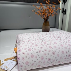 May include: A floral-patterned pillow with pink flowers and gray leaves on a white background. The pillow has a pink border and is on a white bed. The text "春田花开一红" is visible.