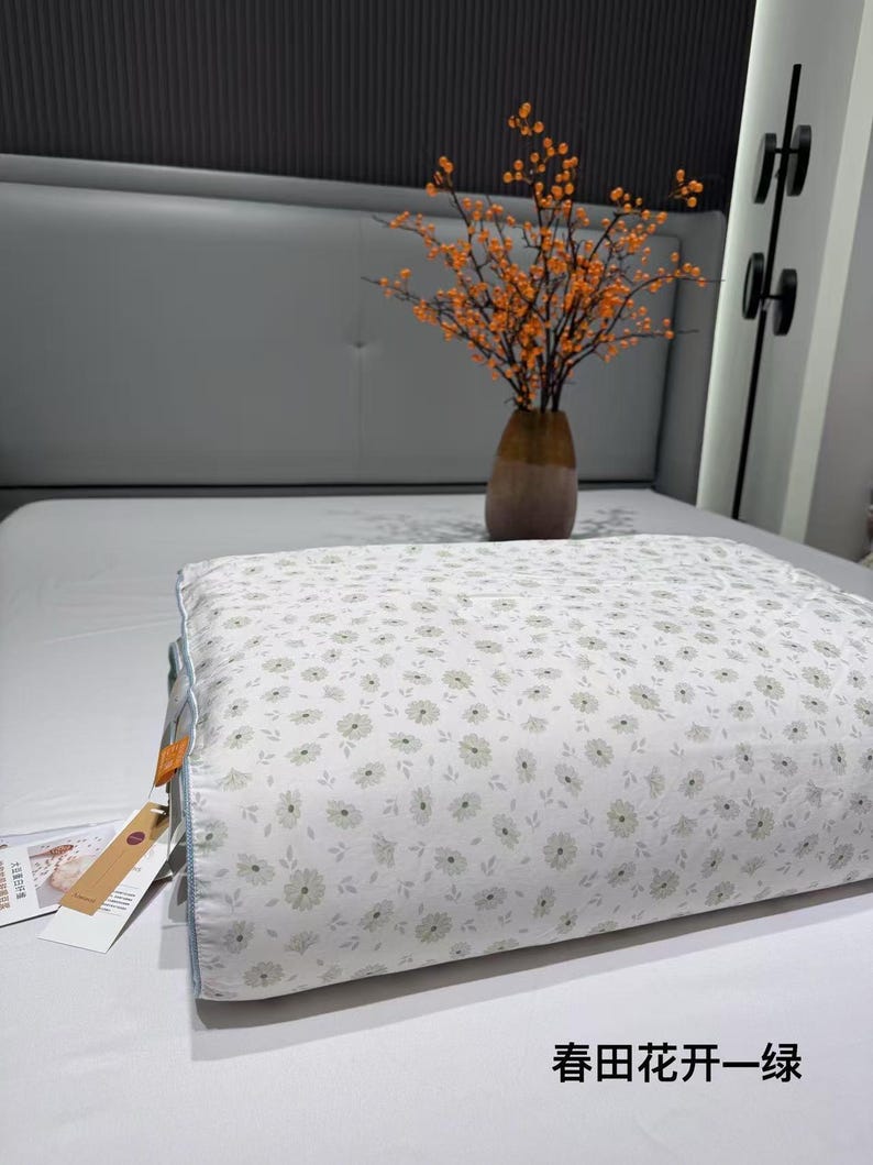 May include: A white pillow with a floral pattern of small, light green flowers. The pillow is on a white bed, with a vase of orange-berried branches in the background. The text "Spring Field Flowers - Green" is visible.