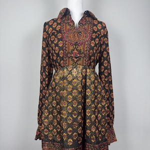May include: A long-sleeved dress with a collared neckline and a button-down front. The dress features a black background with a repeating floral pattern in shades of yellow, red, and green. The dress is displayed on a white mannequin.