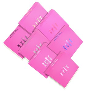 May include: A collection of bright pink custom notebooks, each with the words "Your Custom Text Here" in various metallic colors. The notebooks are arranged in a diagonal pattern against a white background.