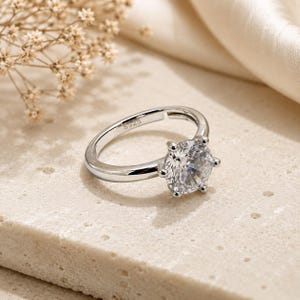 May include: A silver-toned ring featuring a single round, clear, faceted stone held in a six-prong setting. The inner band is clearly engraved with the text S925, indicating the metal composition. The ring has a smooth, polished finish.
