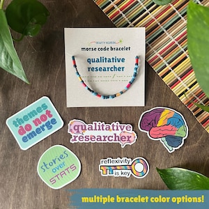 Op de afbeelding: Een morsecode-armband op een displaykaart met het label qualitative researcher, vergezeld van vier stickers met de teksten themes do not emerge, qualitative researcher, stories over stats en reflexivity is key, plus een afbeelding van een brein.