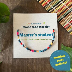 May include: A Morse code bracelet featuring multicolored cylindrical beads on a display card. The card displays the text Crafty Neuron, morse code bracelet, and Master's student, along with a green Morse code pattern and a blue circle with text.