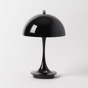 Op de afbeelding: Een zwarte tafellamp met een glanzende afwerking. De lamp heeft een afgeronde kap, een slanke steel en een cirkelvormige voet. Een kleine, zilverkleurige knop bevindt zich bovenop de kap. De lamp is een modern ontwerp.