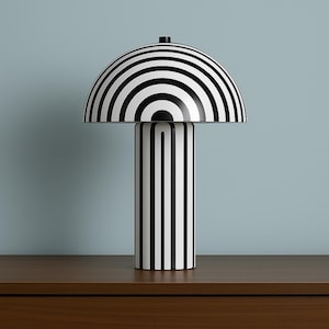 May include: A contemporary table lamp with a striking black and white striped pattern. The lamp has a domed shade and a cylindrical stem, both decorated with vertical stripes. It sits on a wooden surface, set against a pale blue backdrop.