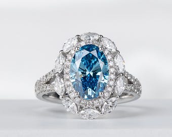 May include: A silver ring with a large, oval-cut, light blue gemstone surrounded by smaller white gemstones. The ring has a halo design with additional gemstones on the band. The ring is displayed on a white surface.