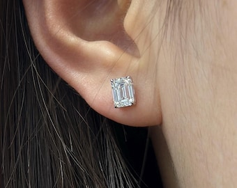 Könnte beinhalten: Nahaufnahme eines Ohrsteckers mit klarem Diamanten im Smaragdschliff. Der Ohrring ist in einer Fassung aus Silber oder Weißgold gefasst und wird an einem Ohr getragen. Der Ohrring ist rechteckig und reflektiert das Licht.