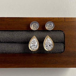 Puede incluir: Un par de pendientes de botón en forma de pera con piedras transparentes facetadas engastadas en biseles de oro amarillo. Los pendientes incluyen dos cierres de silicona translúcida y se presentan en un joyero de madera oscura.