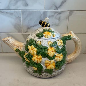 May include: A white ceramic mug with a black handle and the text "But First, Coffee" in a bold, black font. The mug is set against a blurred background, suggesting a cozy setting.