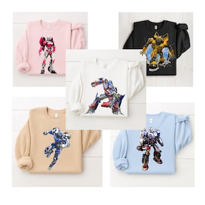 May include: Collection of five crewneck sweatshirts in various colors, each featuring a colorful graphic of a robot character. The sweatshirts are in light pink, black, white, tan, and light blue.