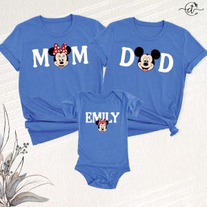 Puede incluir: Camisetas azules a juego para la familia y un body. Las camisetas tienen las palabras "MOM" y "DAD" con caras de Minnie y Mickey Mouse. El body dice "EMILY" con una cara de Minnie Mouse. Las camisetas tienen mangas cortas.