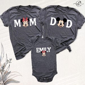 Puede incluir: Tres camisetas grises oscuras y un body para beb&eacute; con Minnie Mouse de Disney. Las camisetas dicen "MOM" y "DAD" con gr&aacute;ficos de Minnie y Mickey Mouse. El body dice "EMILY" con un gr&aacute;fico de Minnie Mouse. Ropa a juego para la familia.