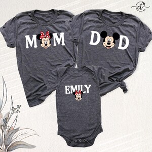 Puede incluir: Tres camisetas grises oscuras y un body para beb&eacute; con Minnie Mouse de Disney. Las camisetas dicen "MOM" y "DAD" con gr&aacute;ficos de Minnie y Mickey Mouse. El body dice "EMILY" con un gr&aacute;fico de Minnie Mouse. Ropa a juego para la familia.