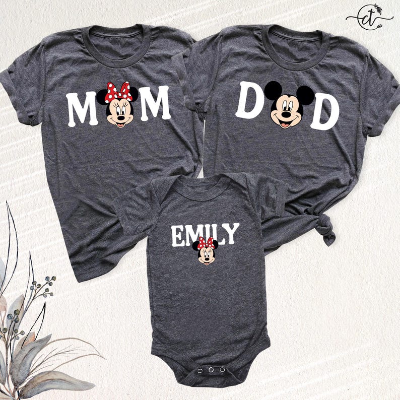 Puede incluir: Tres camisetas grises oscuras y un body para beb&eacute; con Minnie Mouse de Disney. Las camisetas dicen "MOM" y "DAD" con gr&aacute;ficos de Minnie y Mickey Mouse. El body dice "EMILY" con un gr&aacute;fico de Minnie Mouse.