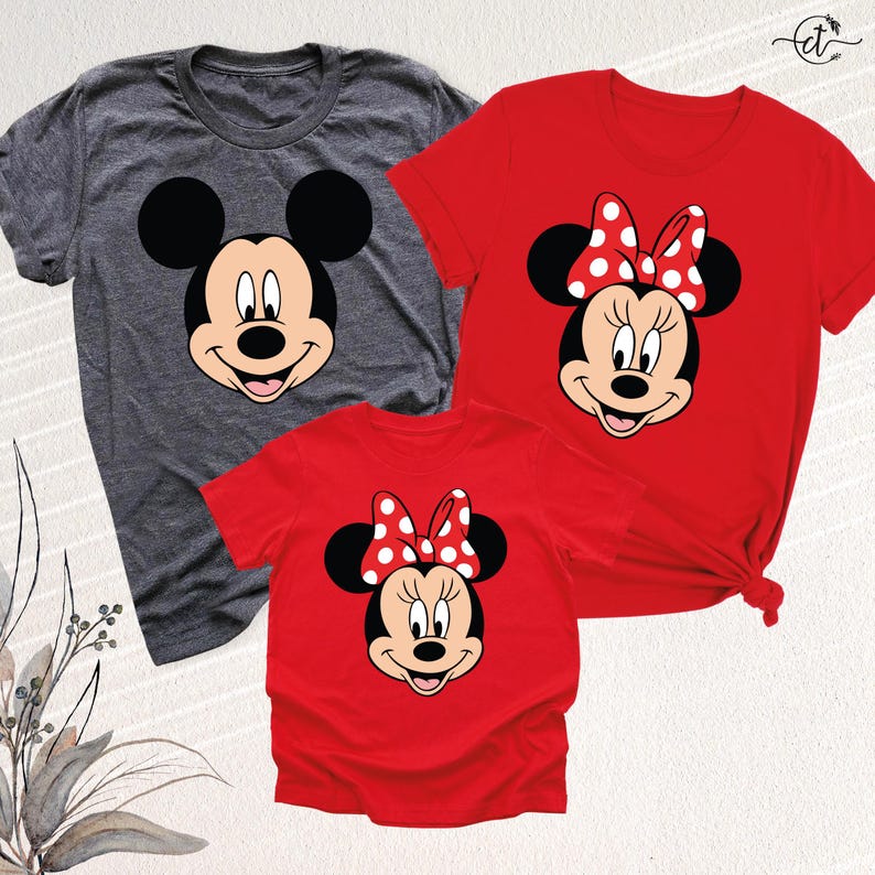 May include: Three t-shirts featuring cartoon character faces. One gray t-shirt displays Mickey Mouse's face, while two red t-shirts showcase Minnie Mouse's face with a polka dot bow. The shirts are short-sleeved.