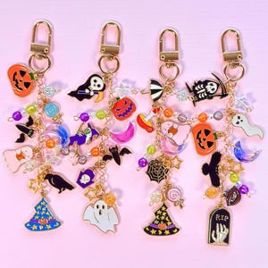 May include: Four gold-toned metal keychains featuring assorted Halloween-themed enamel charms including pumpkins, ghosts, bats, witches' hats, a tombstone with the text RIP, and colorful beads attached to gold chains with lobster claw clasps.