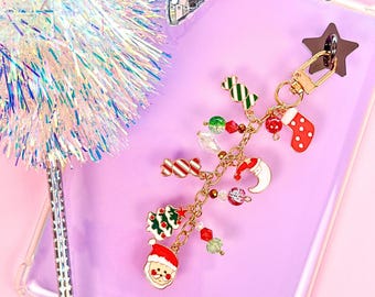 May include: A gold-toned metal keychain featuring a collection of Christmas-themed charms including a Santa Claus face, a decorated tree, a crescent moon with a hat, a red stocking, and candy shapes, interspersed with small red, green, and clear beads.