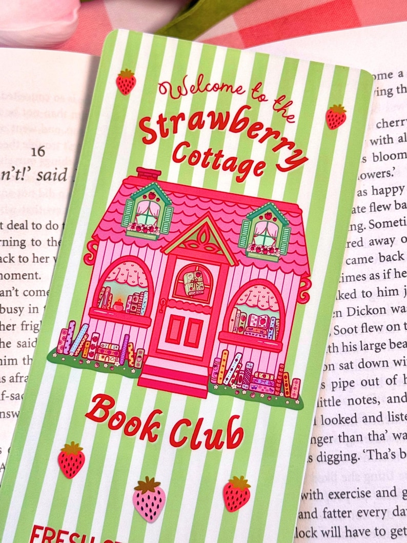 close up of the artwork on the bookmark which has a handdrawn detailed strawberry and book themed cottage, with accents of strawberries and books in the windows and in the front like a row of flowers.
