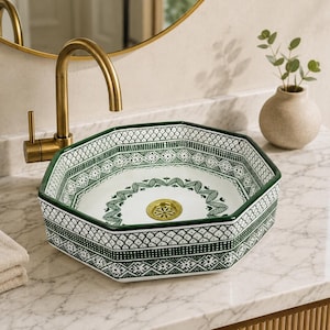 Peut inclure: Une vasque octogonale en céramique présentant une base blanche ornée de motifs géométriques et floraux vert foncé. Le lavabo comprend une bonde dorée et est associé à un robinet doré, le tout posé sur un comptoir en marbre blanc.