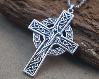 May include: A silver-toned metal pendant in the shape of a Celtic cross, featuring intricate knotwork patterns and a central vine-like design. The cross is layered over a circular ring and hangs from a silver-toned metal ball chain necklace.