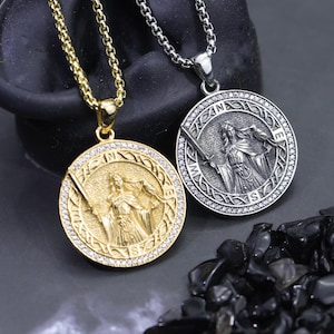 May include: Two round pendants on box chains, one gold-toned and one silver-toned. Each features a central figure holding a sword and a bird, surrounded by a border with the letters N, E, S, and W and a ring of small clear stones.