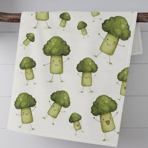 May include: A white kitchen towel with a repeating pattern of cartoon broccoli characters. The broccoli are green with smiling faces and small arms and legs. The towel is hanging on a wooden rod.