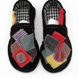 May include: A pair of black slip-on shoes featuring a patchwork design on the uppers with various colored fabric squares, including red, blue, and yellow, accented by visible white stitching and a black and white checkered interior lining.