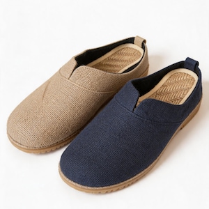 May include: A pair of slip-on shoes featuring one tan and one navy blue textured fabric upper. Each shoe has a rounded toe, a low-cut collar, and a tan rubber sole. The interior footbed displays a woven herringbone pattern in a light tan color.