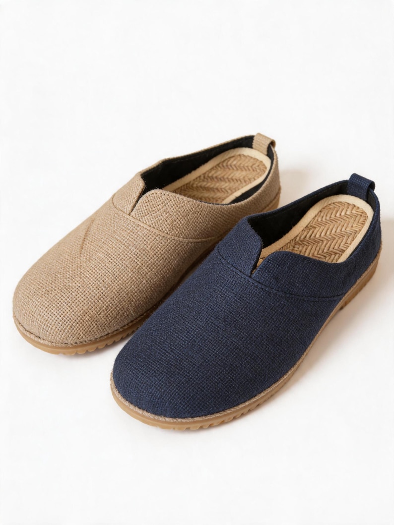 May include: A pair of slip-on shoes featuring one tan and one navy blue textured fabric upper. Each shoe has a rounded toe, a low-cut collar, and a tan rubber sole. The interior footbed displays a woven herringbone pattern in a light tan color.