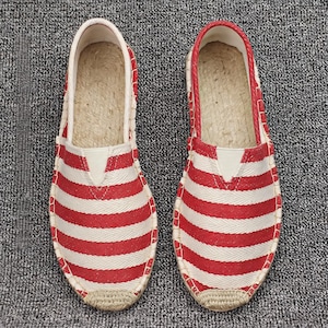 K&ouml;nnte beinhalten: Ein Paar Slipper mit einem rot-wei&szlig;en horizontalen Streifenmuster und Fischgr&auml;tenstruktur. Die Schuhe verf&uuml;gen &uuml;ber eine gewebte Sohlenkante im Jute-Stil und ein helles Innenfutter und sind als leichtes Schuhwerk f&uuml;r den Alltag konzipiert.