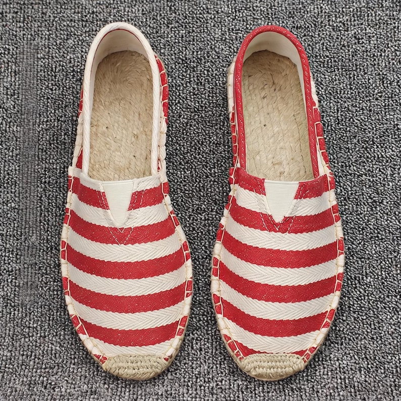 K&ouml;nnte beinhalten: Ein Paar Slipper mit einem rot-wei&szlig;en horizontalen Streifenmuster und Fischgr&auml;tenstruktur. Die Schuhe verf&uuml;gen &uuml;ber eine gewebte Sohlenkante im Jute-Stil und ein helles Innenfutter und sind als leichtes Schuhwerk f&uuml;r den Alltag konzipiert.